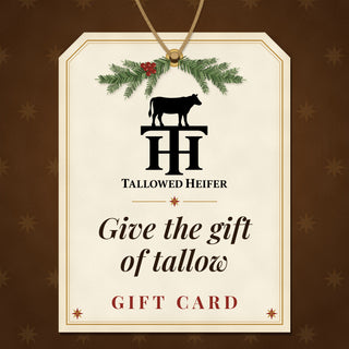 Tallowed Heifer gift card: a cream paper gift tag tied with twine and a sprig of evergreen and red berries, with the Tallowed Heifer cow and TH logo and the words 'Give the gift of tallow' and 'Gift Card'.